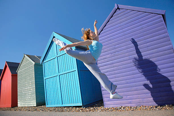 Young Woman Jumping In Front Of Beach Huts Full length of young woman jumping in front of beach huts against blue sky herne bay photos stock pictures, royalty-free photos & images