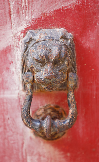 Old weathered and tarnished bronze doorknocker in the shape of a lions head on a grunge red door, close up view