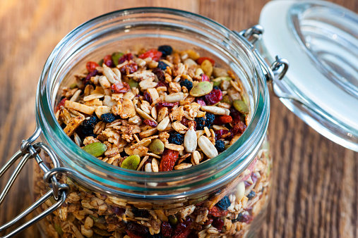 Homemade granola in open glass jar on rustic wooden background