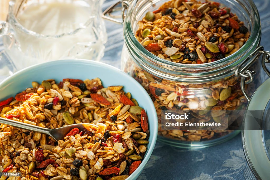 Serving of homemade granola Serving of homemade granola in blue bowl and milk or yogurt on table with linens Berry Fruit Stock Photo