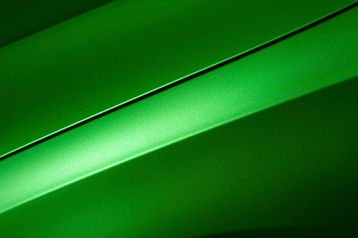 Surface of green sport sedan car, detail of metal hood, fender and door of vehicle bodywork