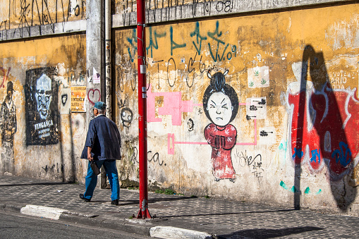 Sao Paulo, Brazil - October 13, 2010: Man walking in front of graffiti wall on street of Liberdade neighborhood. Neighborhood most Japanese immigrants arrived in Brazil in the early twentieth century XX