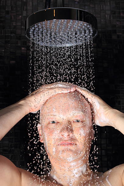 man enjoying a luxury rain shower A man under a luxury rain shower with a dark Italian glass mosaic background. The picture was taken with a high speed flash freezing single water drops. shower men falling water soap sud stock pictures, royalty-free photos & images