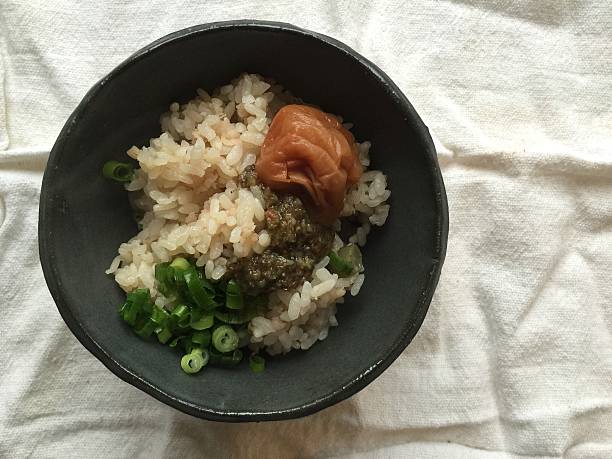 Japanese breakfast of brown rice and toppings Brown rice with a pickled plum (umeboshi) and pickled shiitake mushroom relish in a handmade black clay bowl. genmai stock pictures, royalty-free photos & images