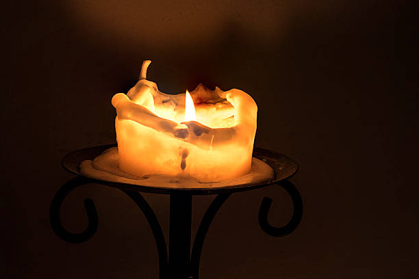 white candle with flame and melting wax, dark background