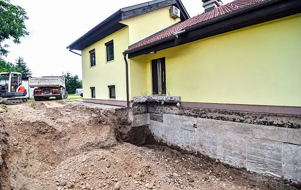 A big family house is being rebuilt with the help of an excavator. Digging the brick foundation for hydro isolation of basement.