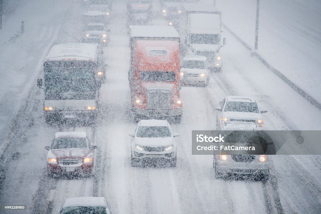 Driving in a Snow Storm Several vehicles are traveling slowly down a multi lane road on an icy stormy day. Snow Stock Photo