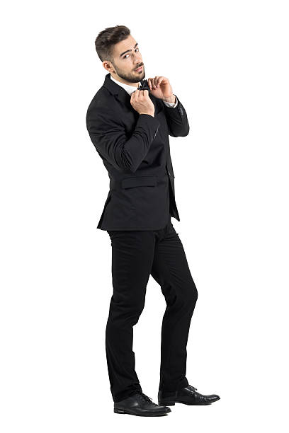 Side view of elegant young male model adjusting bow tie