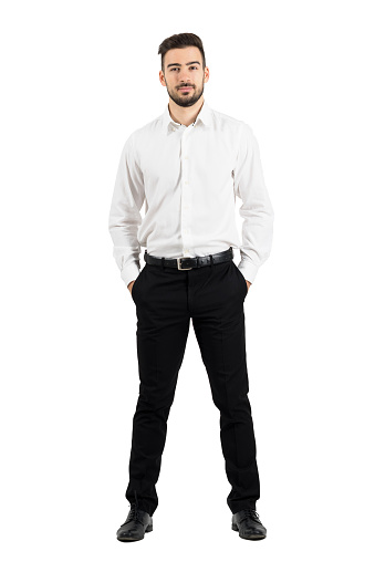 Confident elegant business man with hands in pockets looking at camera. Full body length portrait isolated over white studio background