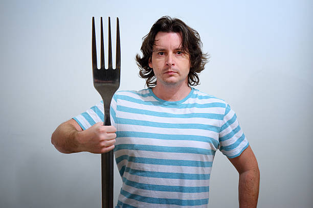 Man with big fork as a Neptune trident White man in blue and white striped t-shirt with big fork in hand as a Neptune trident. Conceptual foto with fantasy aspect for food, healthy style and greece mythology. neptune fork stock pictures, royalty-free photos & images