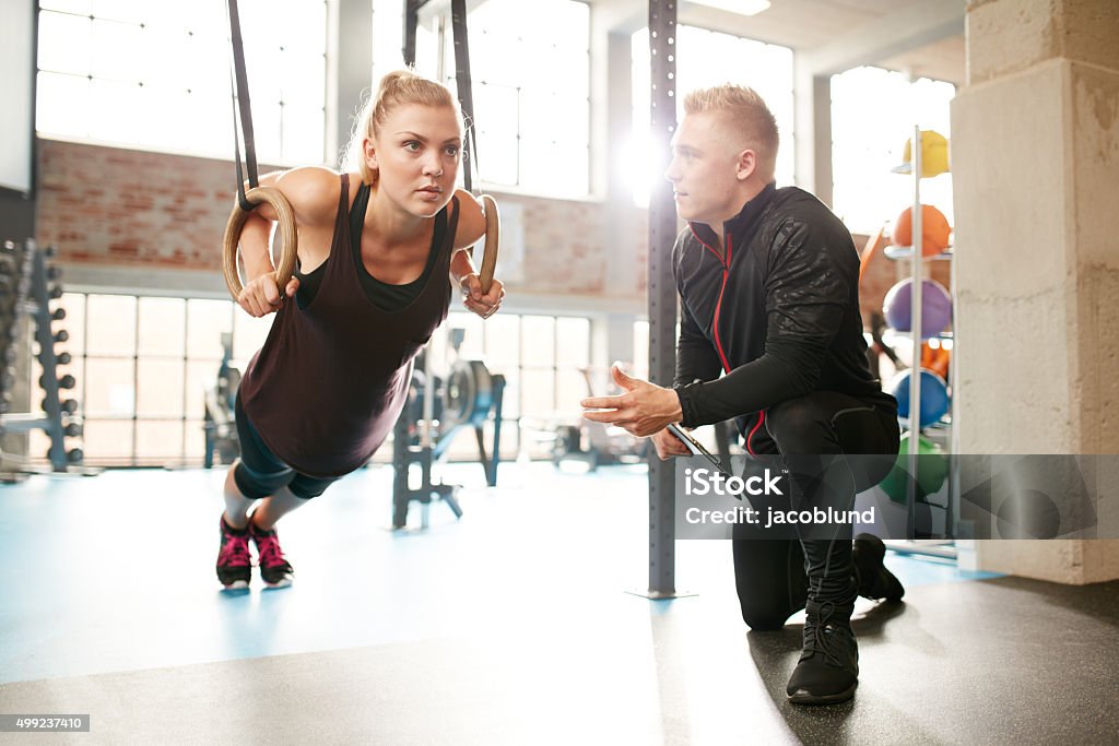 Woman exercising with a trainer at the gym Young woman is doing exercises with the help of a personal trainer in a modern gym. Female working out on gymnastic rings. Fitness Instructor Stock Photo