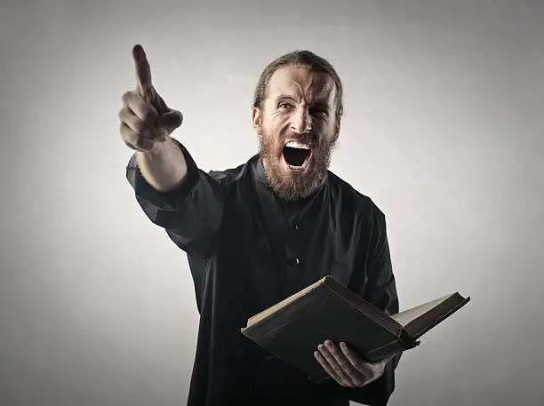 Man dressed as a priest angrily preaching holding the bible in his hand