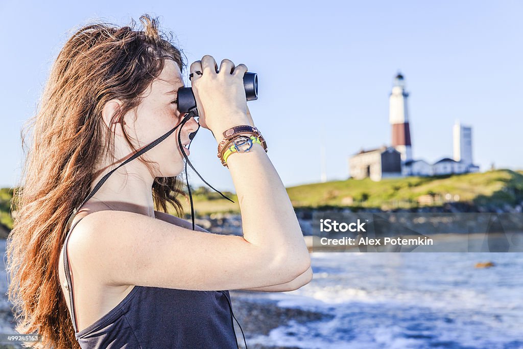 Teenage girl exploring ocean with binocular Teenage girl exploring ocean with binocular in front of Lighthouse at Montauk point, Long Islans. Activity Stock Photo