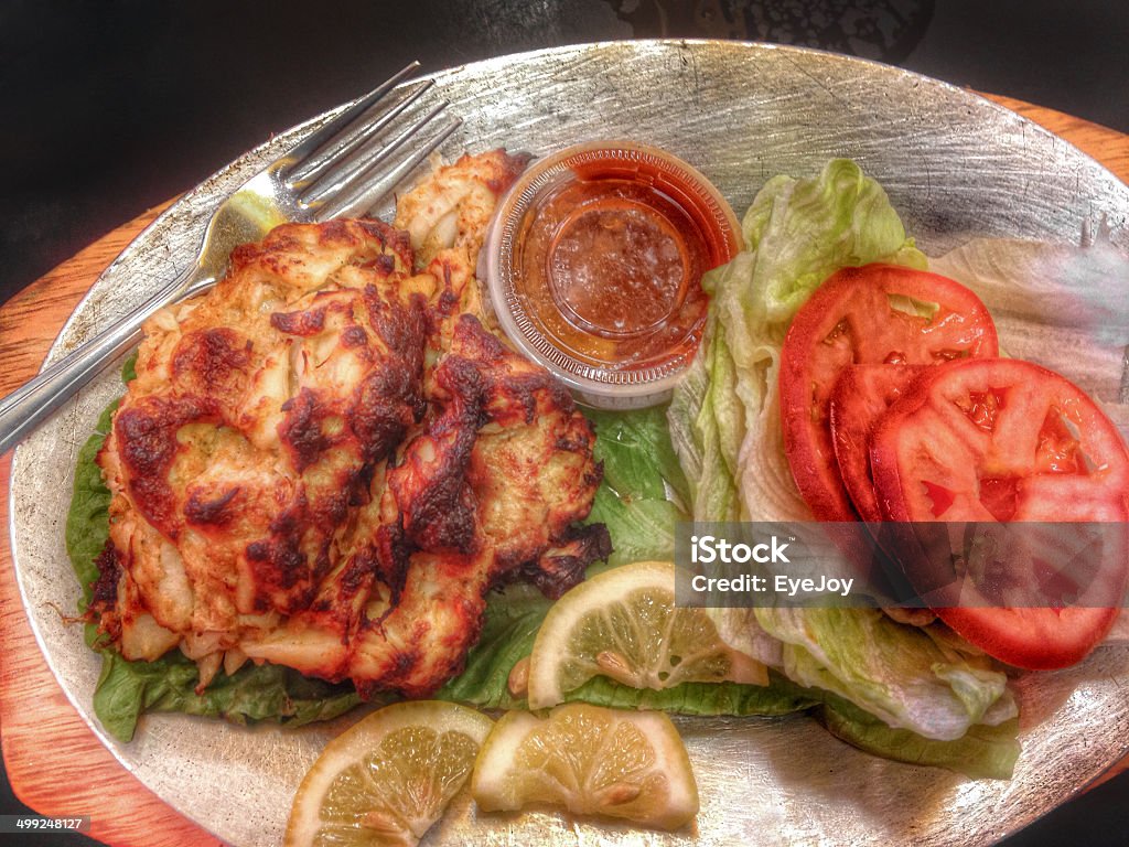 Maryland Crabcake Platter Looking down on close-up of delicious Maryland crabcake lunch platter. Crabcake, tomatoes, lettuce, sauce, lemons. Maryland is known for its delicious seafood, especially crabs and crab cakes. Mobile stock. Breaded Stock Photo