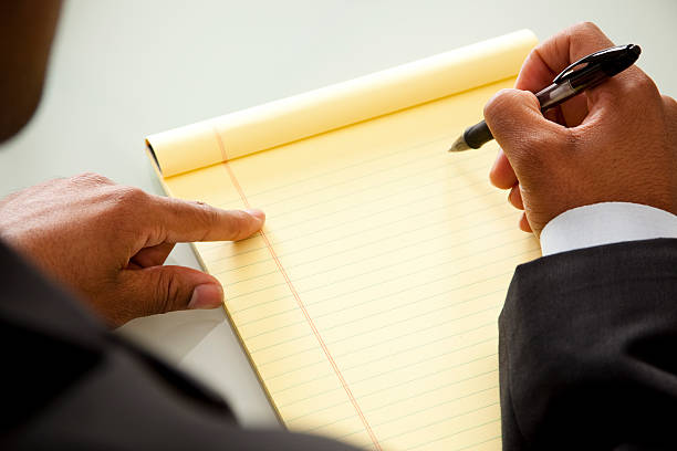 African descent business man uses notepad, pen to take notes during an office meeting.  Blank notepad makes great copyspace.