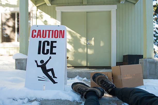 Ice warning sign with feet of fallen delivery person stock photo