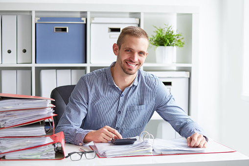 Smiling businessman calculates taxes at desk in office