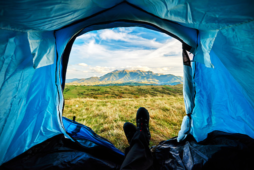 unrecognizable man legs looking at view, relaxing in his tent after mountain climbing, adventure and exploration.