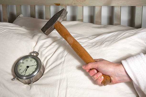 Wake Up Call Hand holding a hammer over an alarm clock on a pillow. smash alarm clock stock pictures, royalty-free photos & images