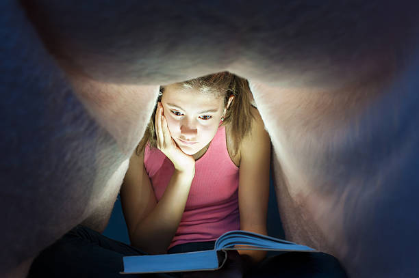 istock Young girl hiding under blanket and enrapt reading interesting book 499282948