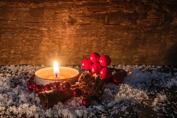 Rustic christmas background with  burning tealight candle,cinnamon, pine cone and cranberries on a wooden table covered with snow.You can use it for a  greeting card or voucher.