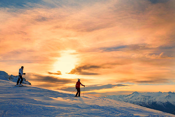 Snow skiers couple  Enjoying a beautiful winter mountains  sunset landscape Snow skiers couple, off piste skiing. Mature women and men enjoying a beautiful winter mountains  sunset landscape. The  orange sky in the background. snow sunset winter mountain stock pictures, royalty-free photos & images