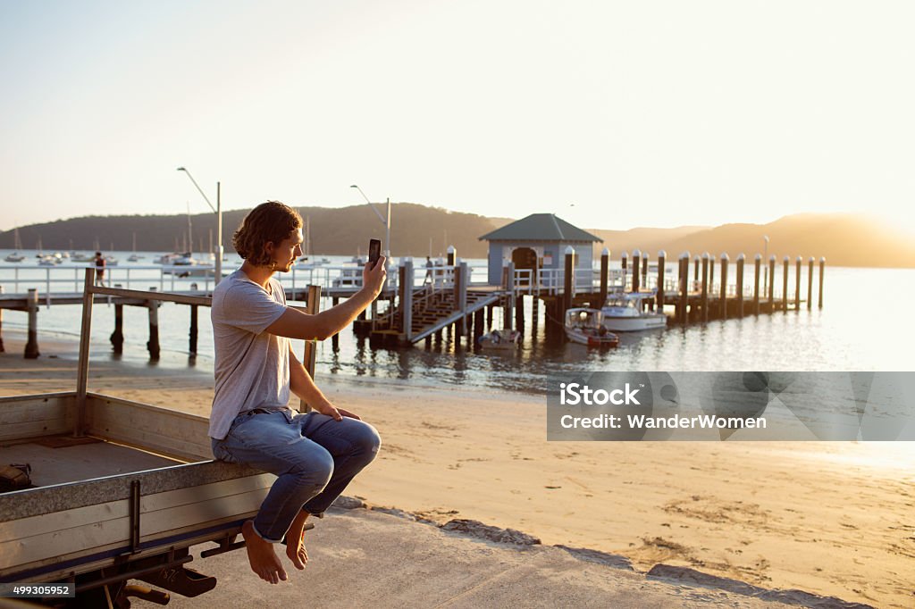Young Australian male taking picture at sunset Young Australian male at Palm Beach Pittwater taking a photo of the sunset Palm Beach - Sydney Stock Photo
