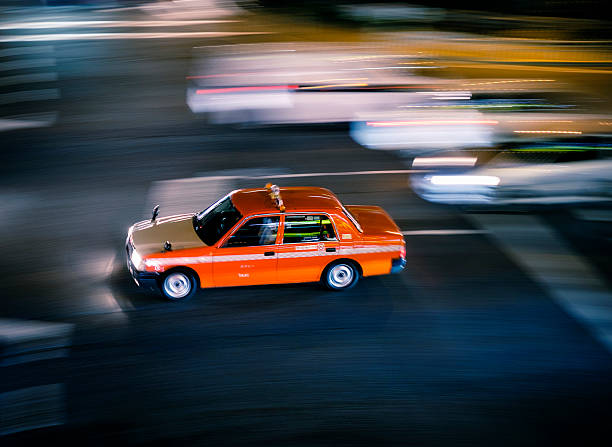 A taxi in Tokyo Japan streaks through in intersection at night. The Japanese writing on the door says \