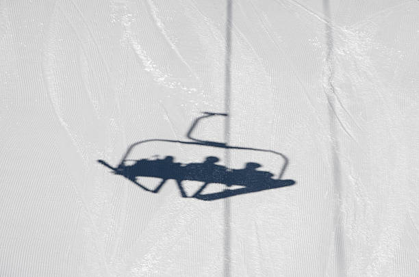The shadow of people riding a ski lift on the bright white snow