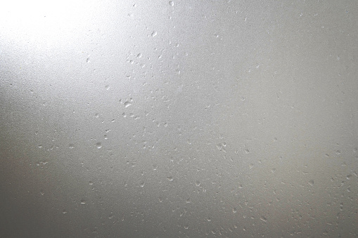 Frosted glass with water drops and bright light at corner