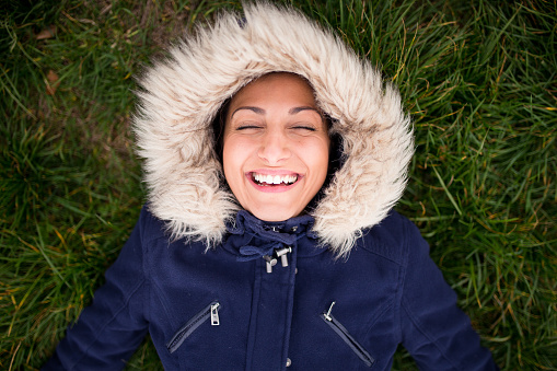 A young woman wearing a fur hood,smiling and lying on the grass,eyes closed,bird eye view