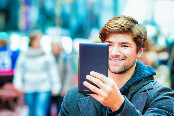 junger mann lächelnd in seinem tablet-pc in städtischen ambiente - digital tablet travel destinations new york state times square stock-fotos und bilder