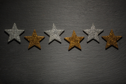 Six silver and golden stars in a row on dark black slate rock background texture.