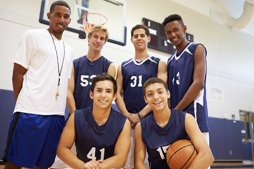 Members Of Male High School Basketball Team With Coach Smiling At Camera