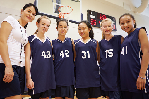 Members Of Female High School Basketball Team With Coach Smiling At Camera
