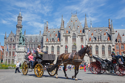 Bruges, Belgium - June 13, 2014: The Carriages on the Grote Markt in full tourist season and the Provinciaal Hof building in background.
