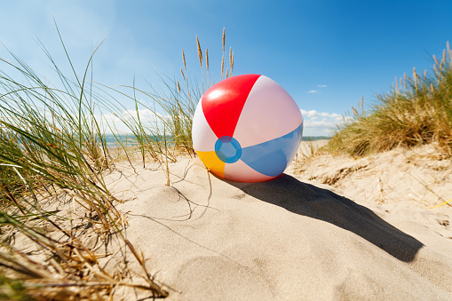 Beach ball resting in sand dune concept for childhood summer vacations, family holiday and healthy lifestyle