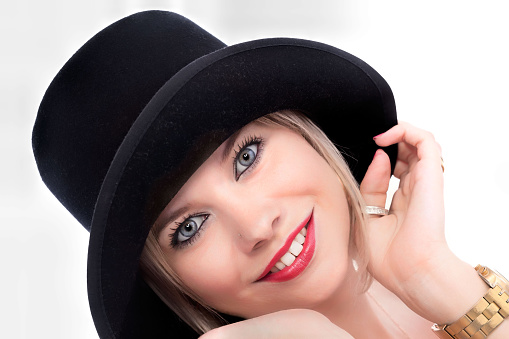 A young beautiful blonde caucasian woman with a short haircut in a beige suit and hat with bouquet of white flowers on blue background. Beauty portrait. The girl smiles, clean skin and white teeth. Beauty portrait.