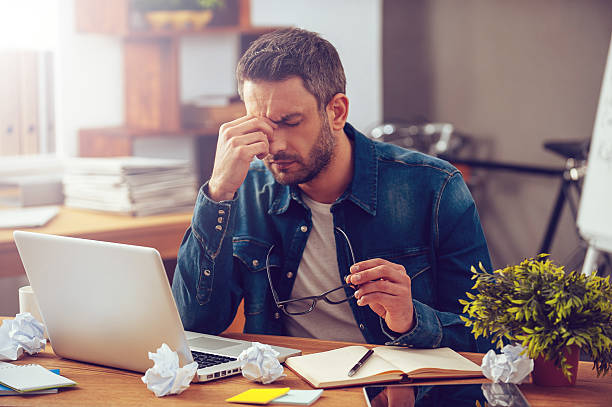 Feeling sick and tired. Frustrated young man massaging his nose and keeping eyes closed while sitting at his working place in office Tensed stock pictures, royalty-free photos & images