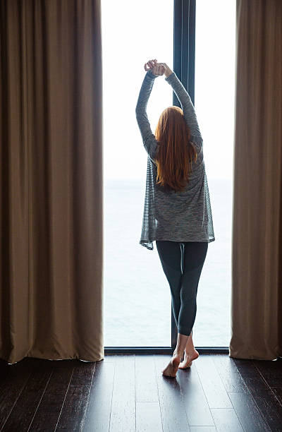 istock Attractive slim lady standing and stretching at the big window 499368752
