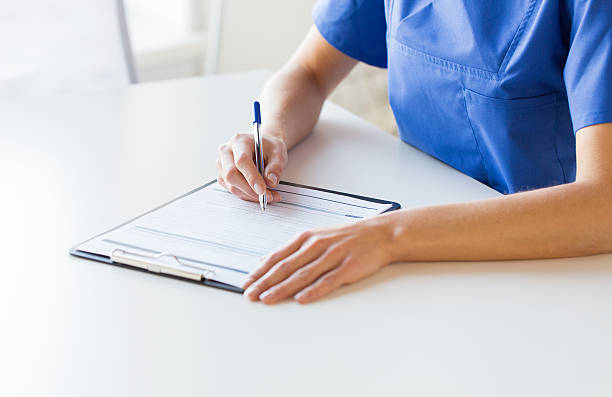 close up of doctor or nurse writing to clipboard stock photo