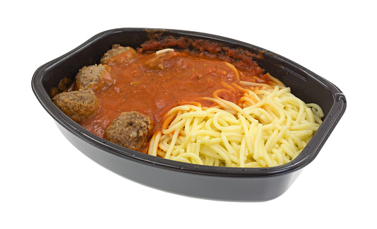 A freshly cooked spaghetti and meatball TV dinner in the black plastic tray on a white background.