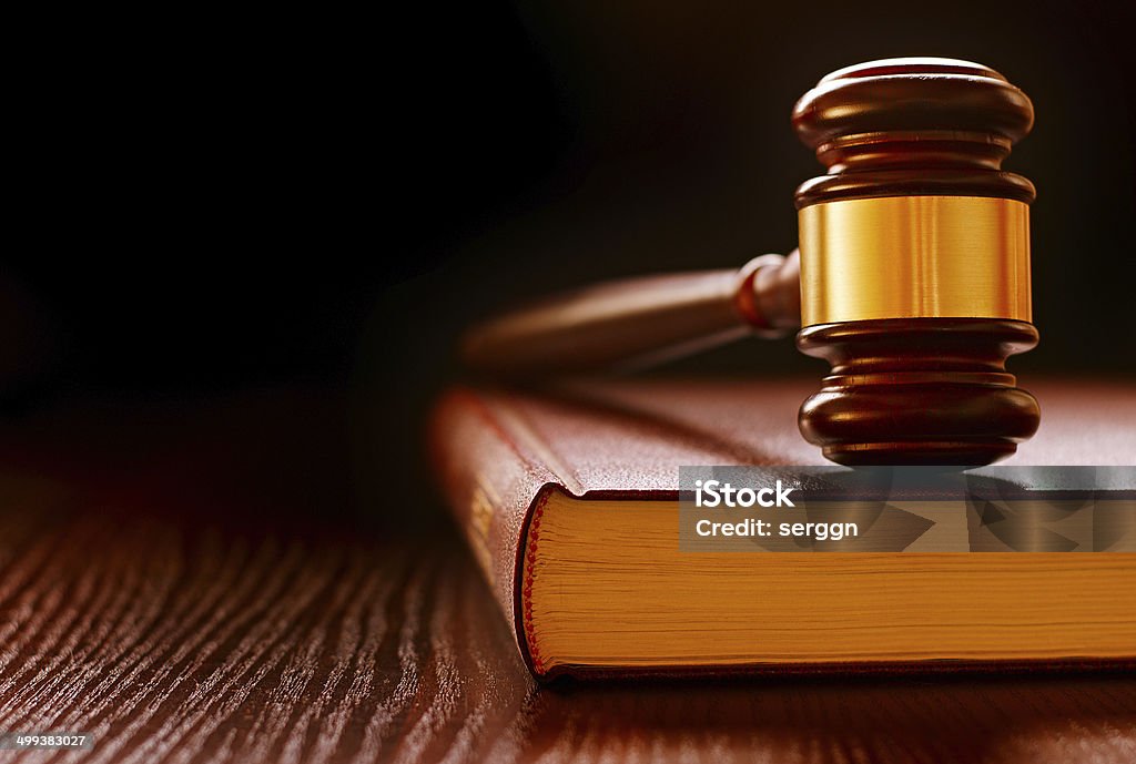 Wood and brass judges gavel on a law book Wood and brass judges gavel standing upright on a law book conceptual of law enforcement and judgements in court Authority Stock Photo