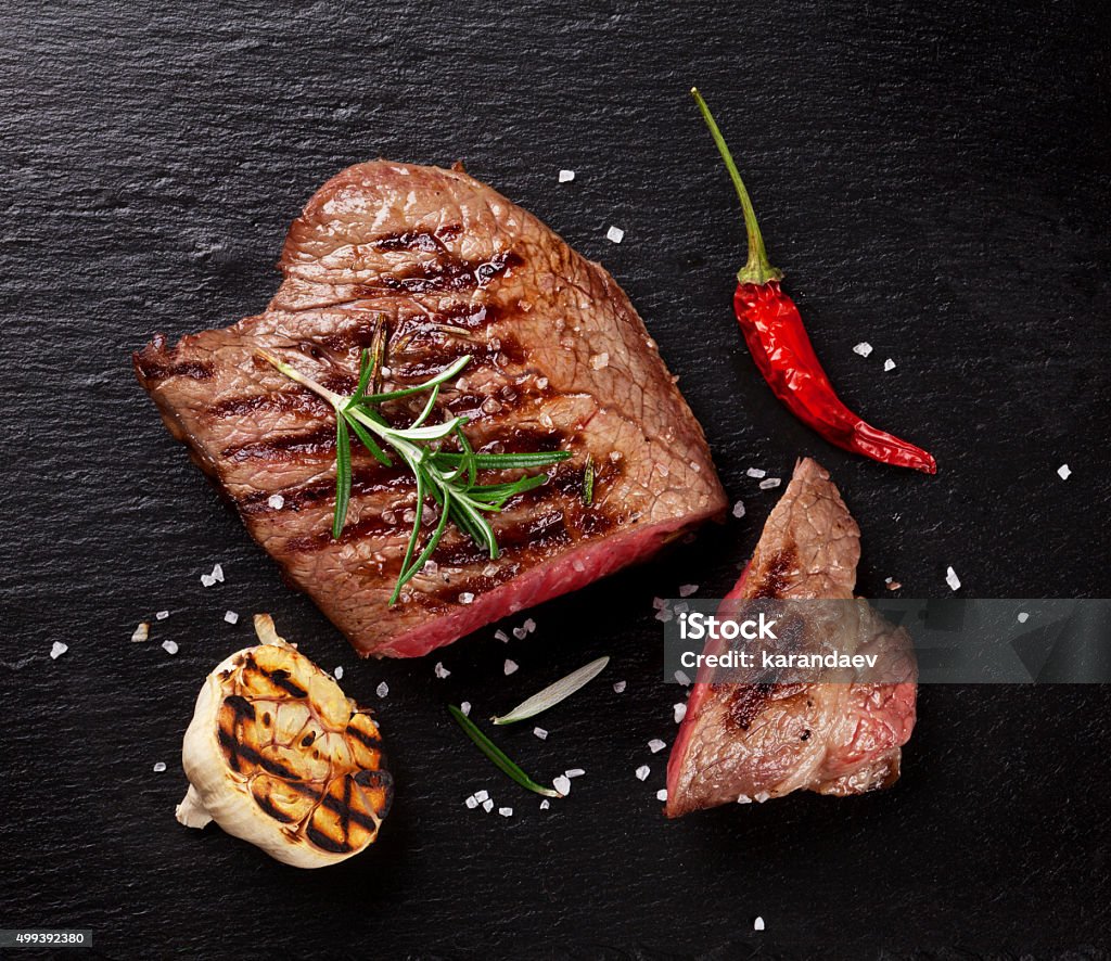 Grilled beef steak with rosemary, salt and pepper Grilled beef steak with rosemary, salt and pepper on black stone plate. Top view Steak Stock Photo