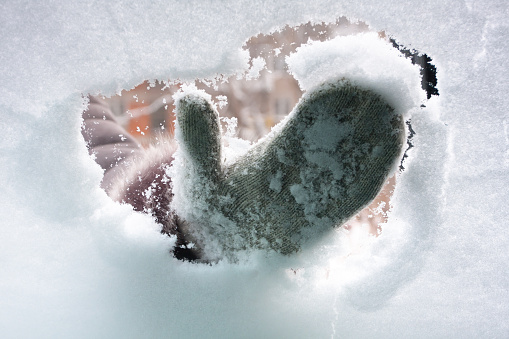 hand in mitten cleaning window of car from the snow, inside view