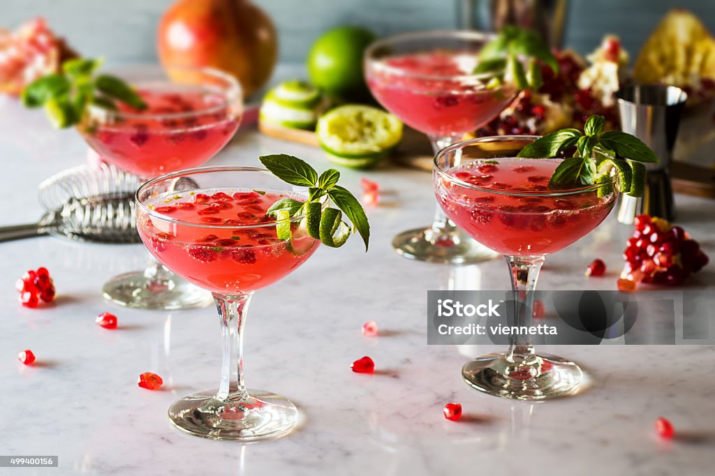 Pomegranate Basil Martinis or Gin Smash Cocktails Pomegranate and basil cocktails with a twist of lime in vintage glasses on a marble countertop. It could be a pomegranate basil martini or a gin smash. Since pomegranates are widely available in the winter, this would be a perfect beverage for holiday parties. Pomegranate Stock Photo