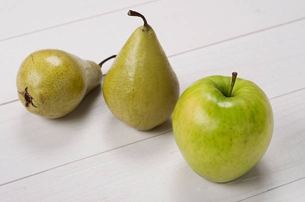 Ripe green apple with pears on a white wooden surface