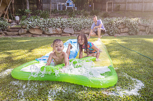 Aboriginal children having fun on the slip 'n slide in the back garden with their father.