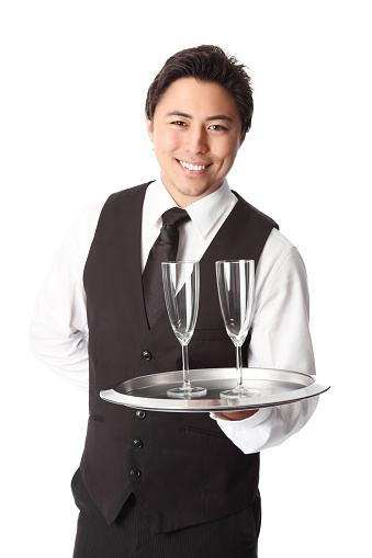 Attractive waiter with 2 empty champagne glasses. Wearing a white shirt and vest. White background.