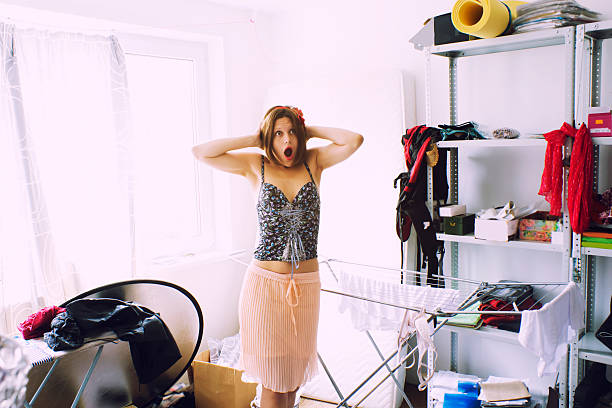 beautiful woman is expressing panic in her really messy room stock photo